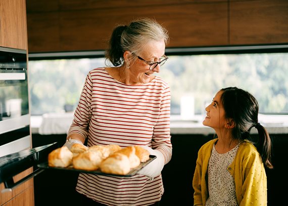 A mature woman holding a tray with pastries and a young girl smiling at her