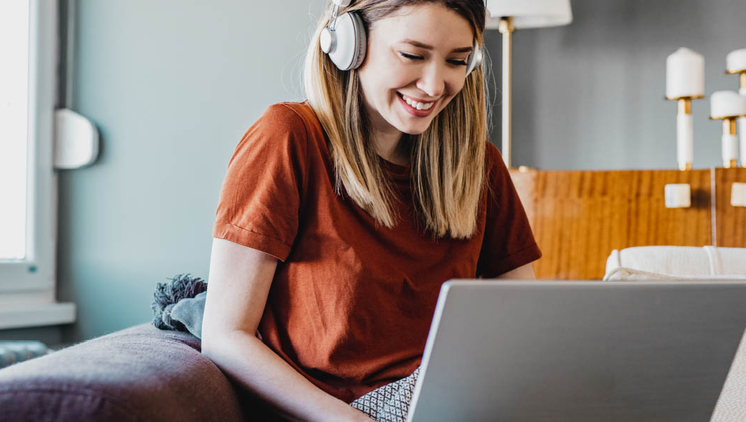 A woman wearing headphones looks at her laptop screen